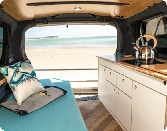 Campervan interior with kitchen units and beach view through the rear