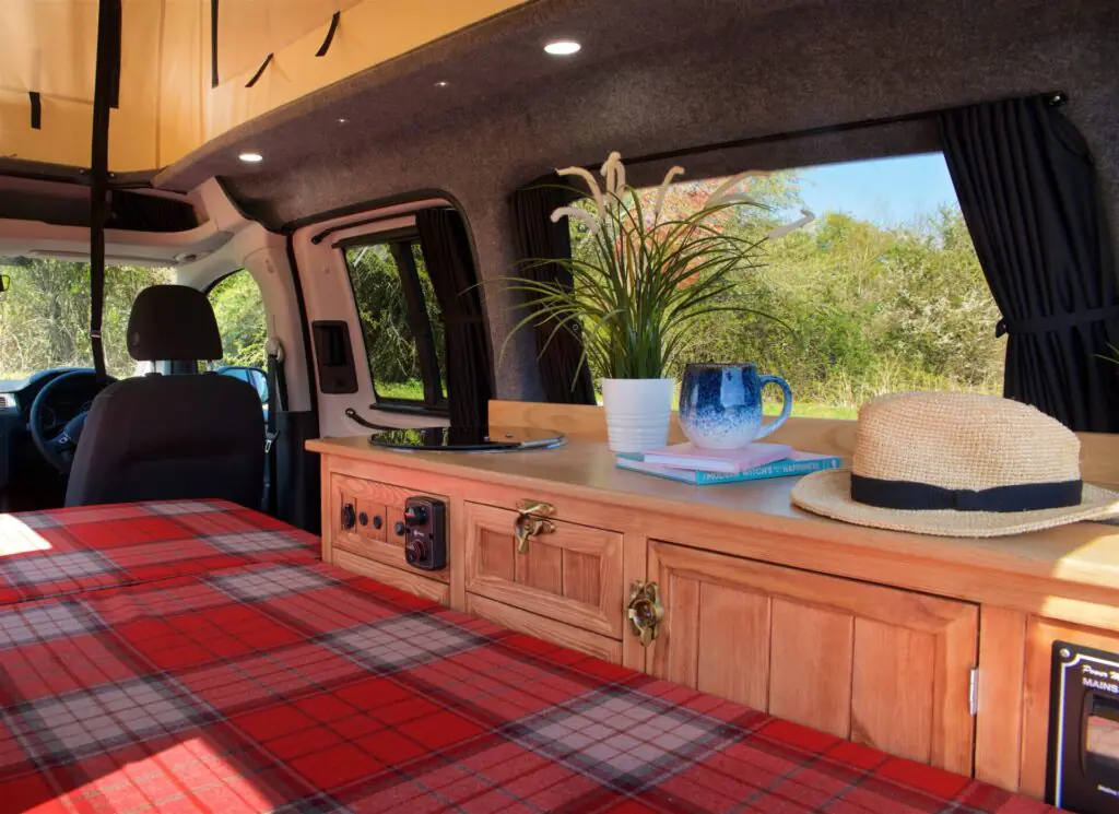 Campervan interior with tartan bed, wooden cabinets and plant