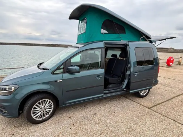 Green VW Caddy campervan with pop-top roof by the sea