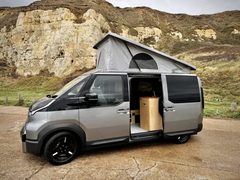 Silver Kia PV5 campervan with pop-top roof by chalk cliffs