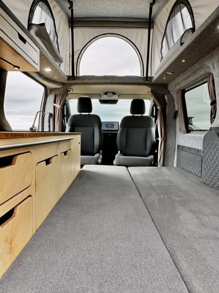 Kia PV5 campervan interior with grey bed and pop-top roof open